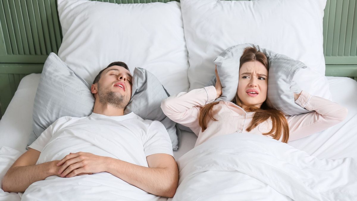 Man snoring in bed, woman covering her ears with a pillow | Intus Healthcare